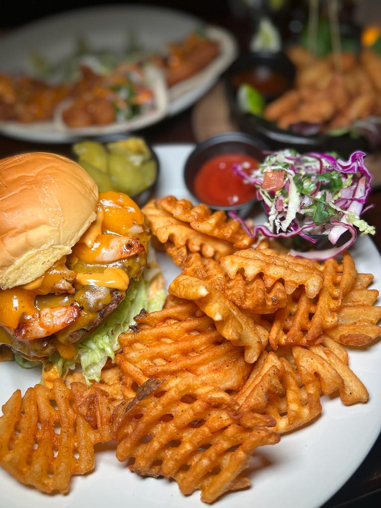 Cheeseburger with melted cheddar, crispy waffle fries, coleslaw, and ketchup on a plate, ideal for burger lovers in a casual dining setting.