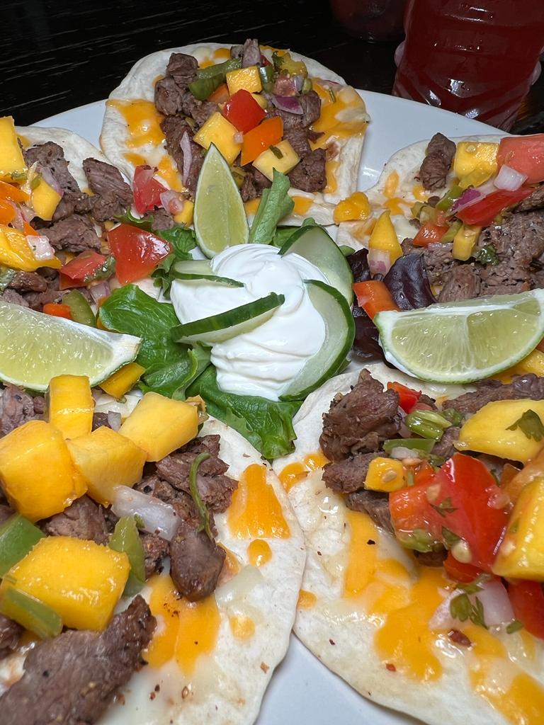 A plate of steak nachos with melted cheese, pico de gallo, mango salsa, and sour cream. Lime wedges are also present