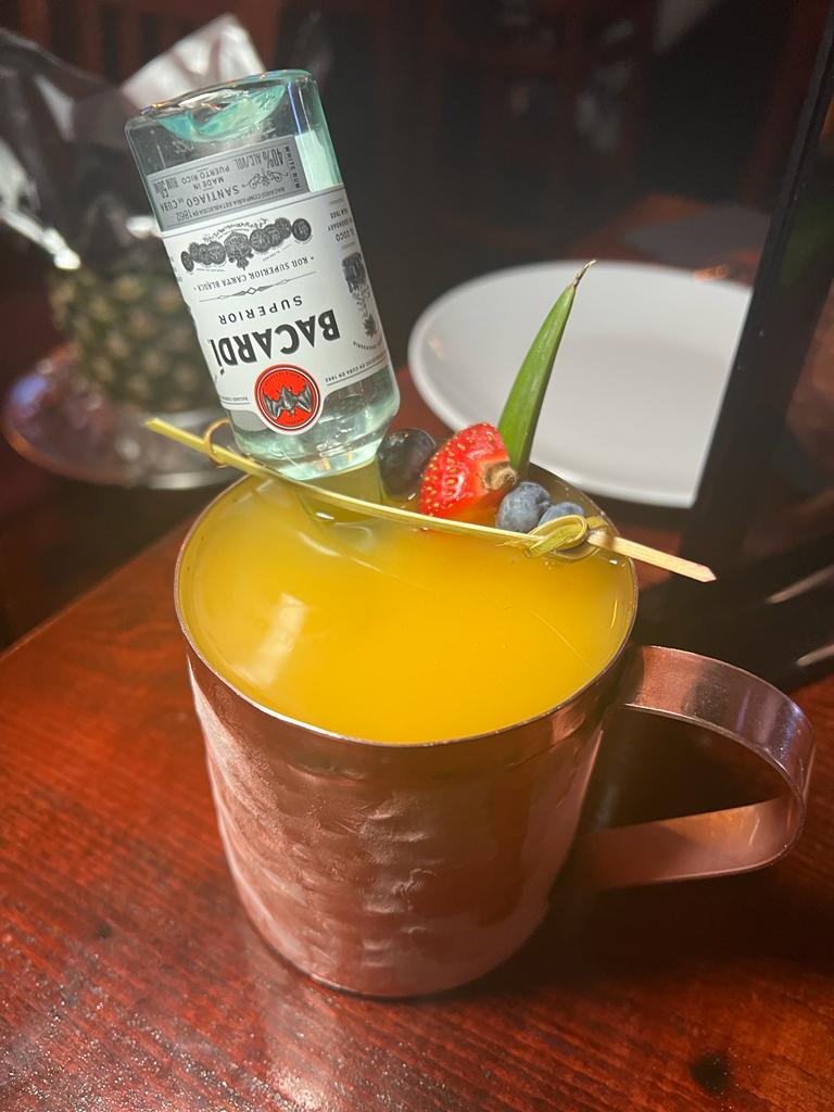 A refreshing cocktail in a copper mug, garnished with fresh berries and a miniature bottle of Bacardi rum