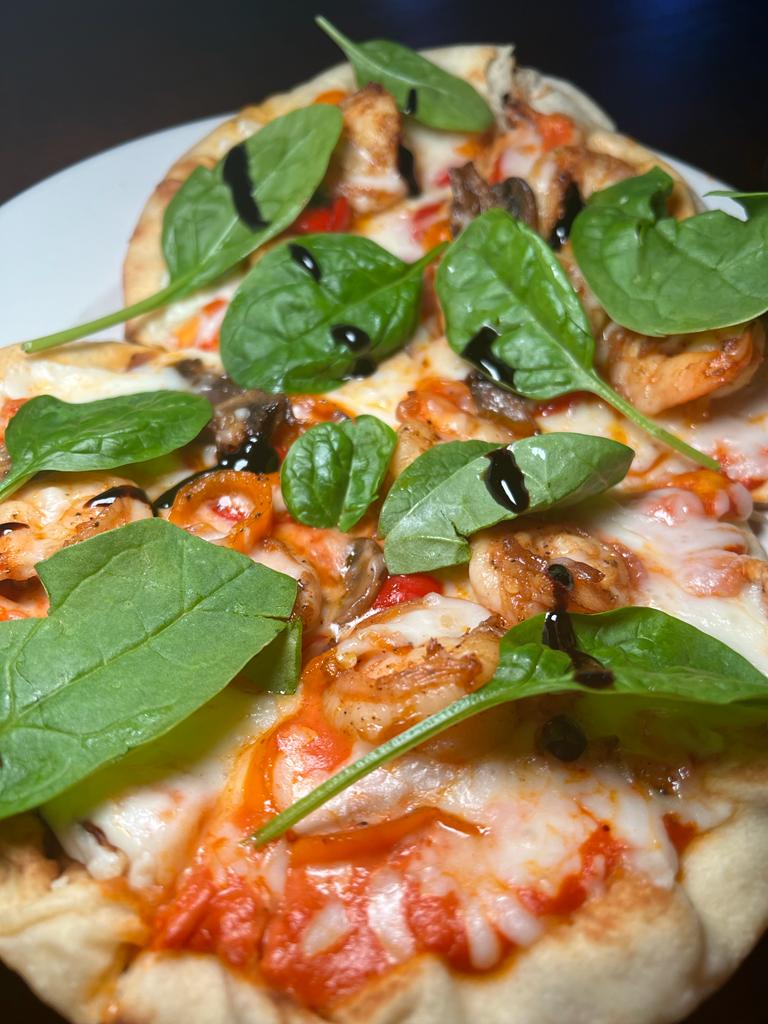 A close-up of a pizza with shrimp, spinach, mushrooms, and a drizzle of balsamic glaze.