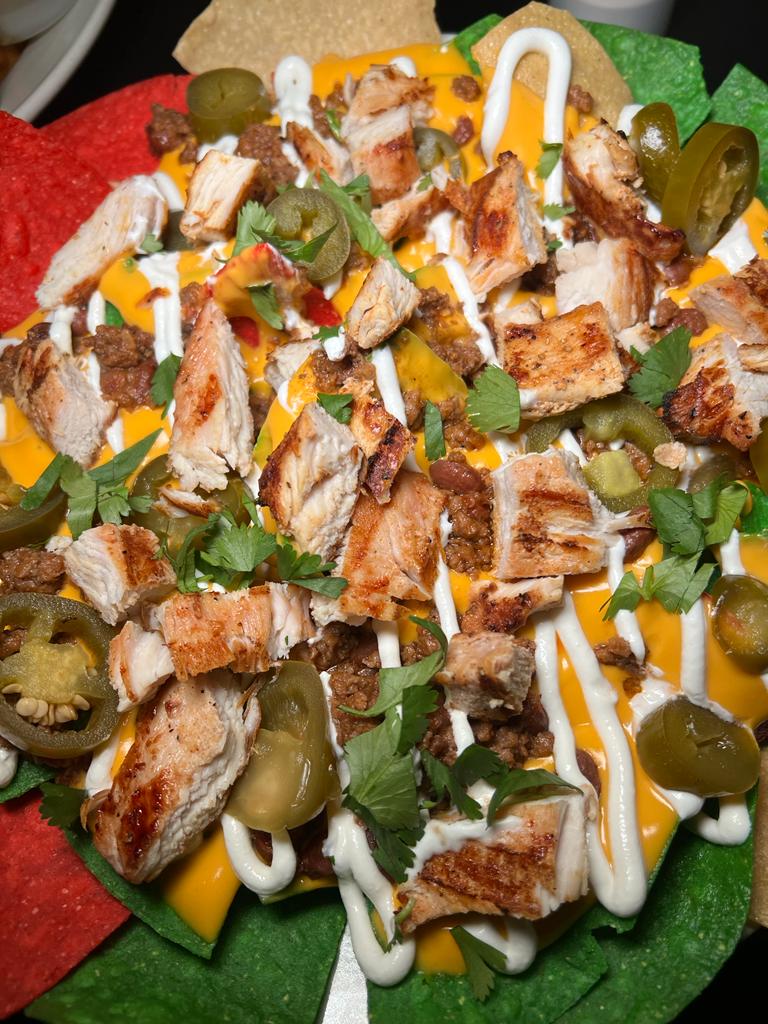 A plate of nachos loaded with cheese, grilled chicken, jalapenos, and cilantro.